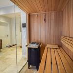 Sauna mit Holzbank und Heizgerät. Durchgehendes Glas trennt den Raum.