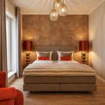 Schlafzimmer mit Bett, zwei Nachttischen, rotem Sessel und Deckenleuchte.