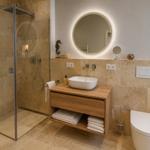 Bad mit Dusche, Waschbecken und Toilette. Holzunterschrank und runder Spiegel.