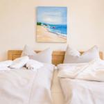 Zwei Betten mit weißen Laken und Kissen. An der Wand hängt ein Strandgemälde.