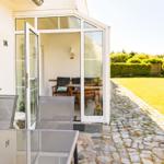 Haus mit Terrasse, Gartentisch und Kiesweg. Durchgehendes Glasdach und grüner Rasen.