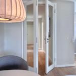 Helle Eingangshalle mit Glas-Türen und Holzboden. Deckenleuchte und Sitzgelegenheit sichtbar.