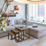 Wohnzimmer mit Sofa, Tisch und Fenster. Blumen im Vordergrund.
