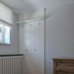 Schlafzimmer mit weißem Schrank, Holzkommode und Fenster mit Rollladen.