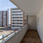 Balcony with tiled floor and railing, overlooking apartment buildings and a red car.