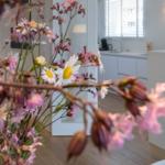 Ein Raum mit Holzboden, weißer Küchenzeile und Blumen im Vordergrund.