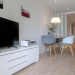 Wohn- und Essbereich mit TV, Tisch und Stühlen. Holzboden und helle Wände.