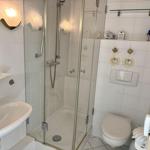 Badezimmer mit Dusche, Waschbecken und Toilette. Weiße Fliesen und Glaswand.