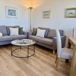 Zwei graue Sofas, runder Tisch, Holzfußboden und Wandbilder.