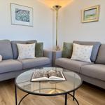 Zwei graue Sofas um einen runden Glas-Tisch mit offenem Buch.