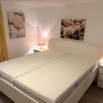 Schlafzimmer mit Doppelbett, zwei Nachttischen und Meeresmuschelbildern an den Wänden.
