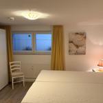 Schlafzimmer mit Bett, Nachttisch, Lampe und Fenster mit gelben Vorhängen.