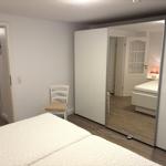 Schlafzimmer mit Bett, Stuhl und Spiegelschrank. Holzdielenboden und Türen im Hintergrund.