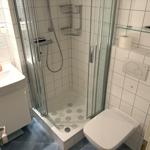 Badezimmer mit Dusche, Waschbecken und WC. Weiße Fliesen und blaue Bodenfliesen.