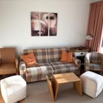 Wohnzimmer mit Sofa, Sessel und Tisch. Wandbild und Fenster mit Vorhängen.