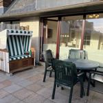 Terrasse mit Strandkorb und Tisch mit Stühlen vor einem Haus mit Glasfront.