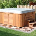 Ein Whirlpool mit Holzrahmen und Auflage auf einer Terrasse im Garten.