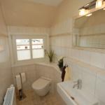 Badezimmer mit Toilette, Waschbecken und Fenster. Fliesenwand und Boden.