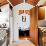 Kitchen with wooden ceiling and view into bedroom with bed and wall art.