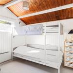 Room with bunk bed, dresser, and window. Wooden ceiling and white walls.
