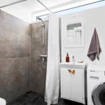 Shower with curtain, sink and washing machine against white wall.