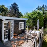 Black wooden house with terrace, table, chairs, and umbrella. Surrounded by trees and greenery.