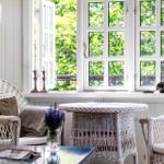 Living area with white wicker furniture and view of green trees through windows.