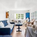 Living room with blue sofa, wicker chairs, and wooden floor. Windows with view of greenery.