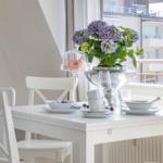 Esstisch mit Stühlen, Blumen und Geschirr vor Fenster