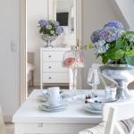 Esstisch mit Stühlen, Blumen und Geschirr. Im Hintergrund Schrank und Spiegel.