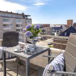 Terrasse mit Tisch, zwei Stühlen und Blumen. Blick auf Wohngebäude und Straßen.