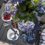 Tisch mit Blumen, Kirschen und Geschirr auf Terrasse