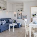 Wohn- und Essbereich mit blauem Sofa, weißem Tisch und Stühlen sowie Küchenregalen an der Wand.
