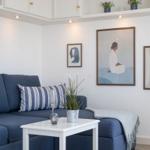 Ein Wohnzimmer mit blauem Sofa, weißem Tisch und Wandbildern.