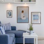 Ein Wohnzimmer mit blauem Sofa, weißen Möbeln und Bildern an der Wand.