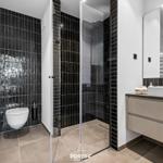 Moderne Badewanne mit Dusche, Toilette und Waschtisch. Schwarze Fliesen und Spiegel.