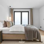 Schlafzimmer mit Bett, Nachttisch und Fenster. Holzboden und helle Wände.