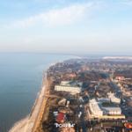 Aerial view of coastal town with beach, houses, and distant dunes.