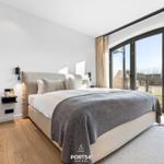 Schlafzimmer mit großem Bett, Holzboden und bodentiefen Fenstern mit Blick nach draußen.