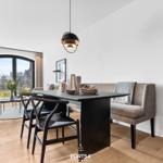 Essbereich mit Tisch, Stühlen und Sofa. Große Fenster mit Blick auf Außenbereich.