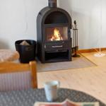 A wood-burning stove stands in a room with wooden floor and table in the foreground.