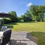 Terrace with table, chairs, and umbrella. Lawn and trees in the background.