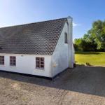 A white house with red window frames and a black roof on a gravel area.