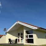 Ein gelbes Ferienhaus mit Terrasse, Tisch und Stühlen. Hintergrund: klarer Himmel.