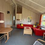 Wohn- und Essbereich mit rotem Sofa, Holztisch und Fenster mit roten Vorhängen.