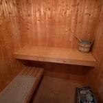 Sauna mit Holzwand, Bank, Eimer und Steinbecher.