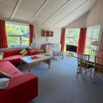 Wohn- und Essbereich mit rotem Sofa, Holztisch und TV. Rote Vorhänge und Holzwände.