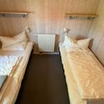 Zwei Einzelbetten mit Bettwäsche und Decken in einem Raum mit Holzwänden und Regalen.