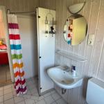Badezimmer mit Waschbecken, Spiegel und Dusche mit buntem Vorhang.