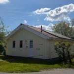 Ein gelbes Haus mit rotem Dach, umgeben von Grün und Bäumen unter blauem Himmel.